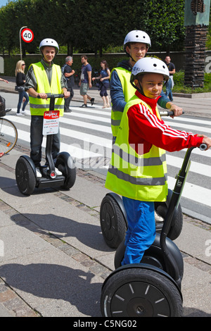 Giovani turisti in giallo giubbotti di sicurezza e caschi con ricevitore radio su Segway in giro per la città di Copenhagen, Danimarca Foto Stock