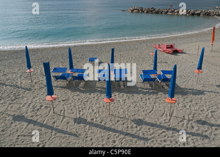 Sedie a sdraio e ombrelloni sono allineate in modo ordinato sulla spiaggia, al mattino presto prima di andare in spiaggia, con lunghe ombre portate. Foto Stock
