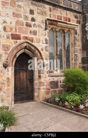 Chiesa della Santa Trinità, Skipton - primo piano esterno della porta, porta in legno, arco in pietra intagliato, vetrine e giardino di cortile - Yorkshire, Inghilterra, UK. Foto Stock