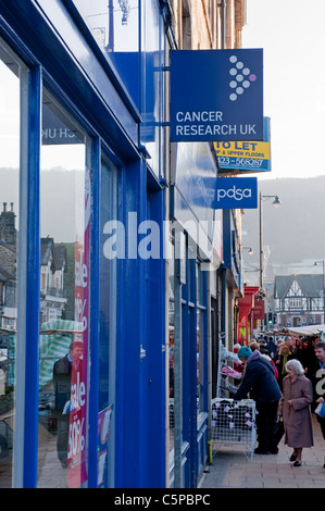 Strada alta trafficata durante il giorno del mercato invernale, la gente che acquista alle bancarelle e fila dei negozi di beneficenza (Cancer Research UK, PDSA) - Otley, West Yorkshire, Inghilterra. Foto Stock
