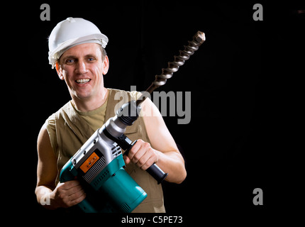 Il builder in un casco di protezione contiene il Professional Puncher-martello con una punta da trapano del diametro di grandi dimensioni Foto Stock