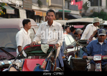 Un ciclo taxi driver si pedala su una strada trafficata con traffico pesante in Phnom Penh Cambogia. Foto Stock