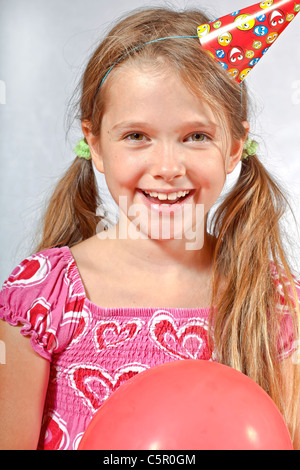 8 anno vecchia ragazza con party hat e tromba su un festival dei bambini Foto Stock
