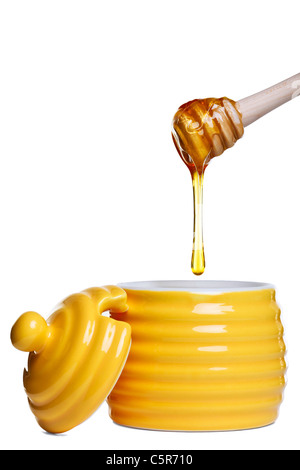 Foto di un giallo a forma di alveare honey pot con gocciolamento bilanciere mantenuto al di sopra, isolato su uno sfondo bianco. Foto Stock