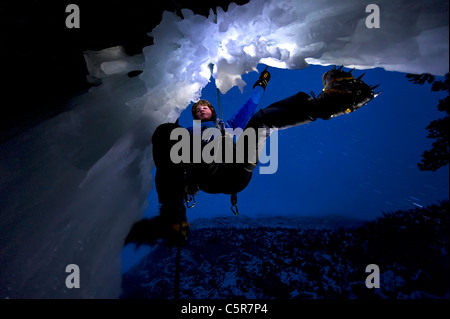 Arrampicata su ghiaccio di notte sul bordo di una grotta. Foto Stock