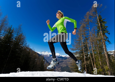 Una donna jogging attraverso innevate montagne d'inverno. Foto Stock