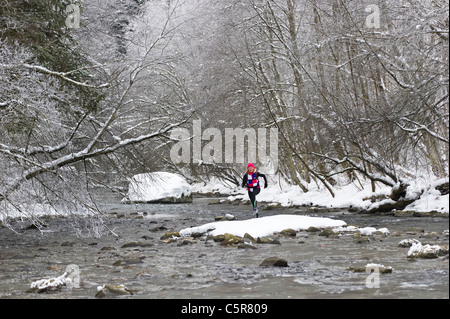 Un pareggiatore attraversando un nevoso fiume alpino Foto Stock