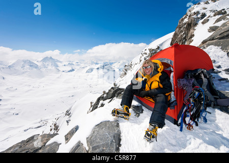 Un felice alpinista seduto alla porta della sua tenda Foto Stock