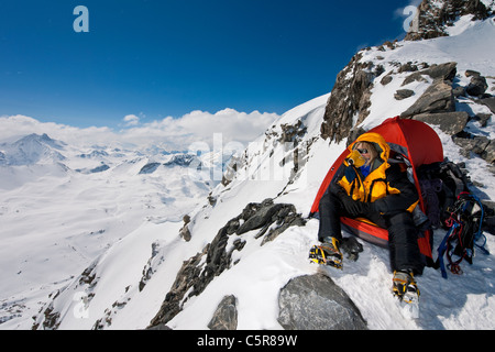 Un alpinista seduto in tenda con le maschere di ossigeno si affaccia su alte montagne innevate. Foto Stock