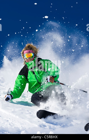 Una femmina di sciatore sorrisi come ella gli sci duro attraverso l esplosione di polvere di neve. Foto Stock