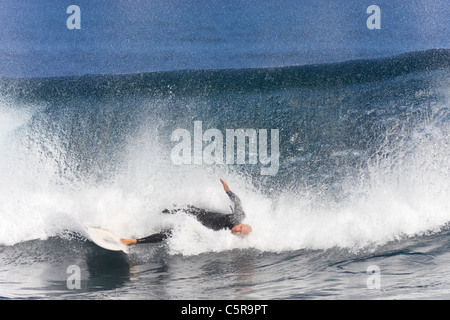 Grande onda si blocca verso il basso sul surfer che ha ancora un piede sulla tavola da surf. Foto Stock