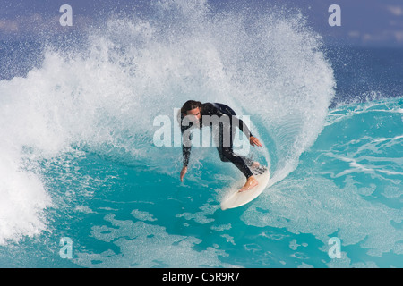 Surfer passeggiate lungo blu azzurro onda. Foto Stock