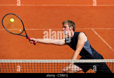 Un giocatore di tennis al netto si allunga per giocare a palla. Foto Stock