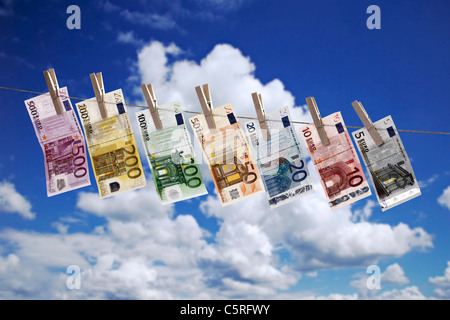 Diverse banconote in euro appesi stendibiancheria contro il cielo nuvoloso Foto Stock