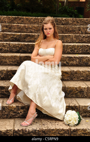 Un 20 qualcosa bionda sposa caucasica è seduto sui gradini di pietra inla chiesa dopo essere stato sorgeva fino al suo matrimonio. Foto Stock