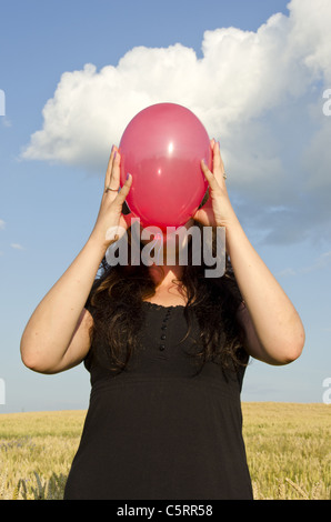 Giovane donna vestita con abito nero, tenendo il palloncino rosso nella parte anteriore del suo volto. Foto Stock