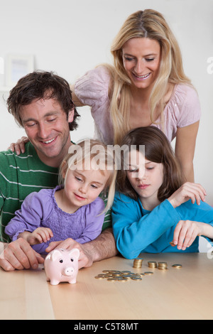 In Germania, in Baviera, Monaco di Baviera, Famiglia con monete e salvadanaio, sorridente Foto Stock