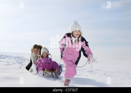 In Germania, in Baviera, Monaco di Baviera, ragazza (8-9) tirando la sorella (4-5) sulla slitta, madre in background Foto Stock