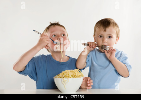 Due ragazzi (6-7) (2-3) Mangiare spaghetti, ritratto Foto Stock