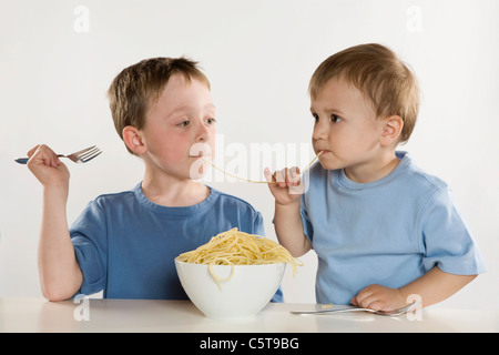 Due ragazzi (6-7) (2-3) Mangiare spaghetti, tagliatelle di condivisione, ritratto Foto Stock