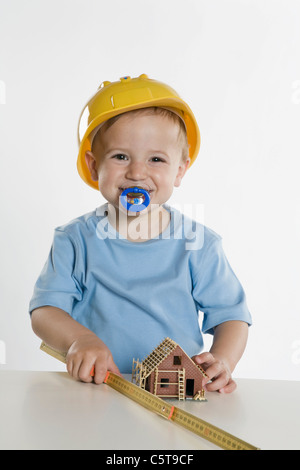 Ragazzo (2-3) INDOSSARE ELMETTO, giocando con il regolo pieghevole Foto Stock