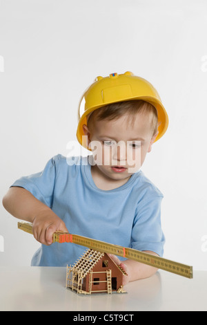 Ragazzo (2-3) INDOSSARE ELMETTO, giocando con il regolo pieghevole Foto Stock