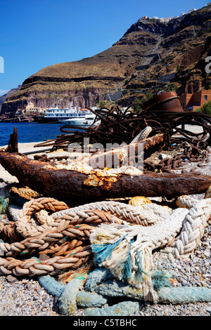 Santorini isola greca, Cicladi Grecia, vecchio arrugginito ancoraggio della nave e la corda a terra con la nave di crociera dietro Foto Stock