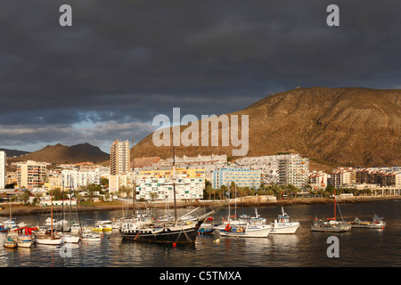 Spagna Isole Canarie, Tenerife, Los Cristianos, vista delle barche in acqua con gli edifici e le montagne sullo sfondo Foto Stock