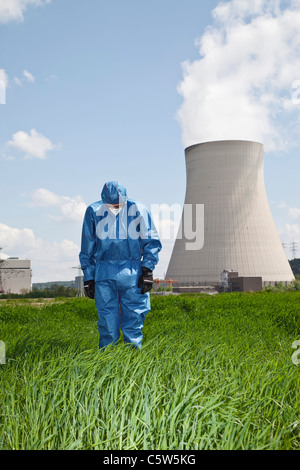 In Germania, in Baviera, Unterahrain, uomo con indumenti da lavoro protettiva in piedi e guardando verso il basso nel campo A AKW Isar Foto Stock