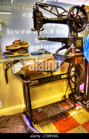 Immagine hdr di una cantante in macchina da cucire in una cobblers shop con i lavori in attesa di essere riparato, riparatori, borsa, scarpe, antichi Foto Stock