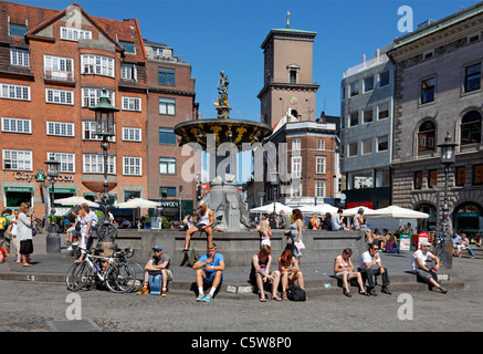 I turisti si rilassano sulla fontana della Caritas a Gammeltorv su Strøget, nella città di Copenaghen, in una calda e soleggiata giornata estiva. Higge danese. Foto Stock