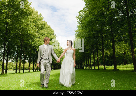 In Germania, in Baviera, la coppia di sposi nel parco camminando mano nella mano, sorridente, ritratto Foto Stock