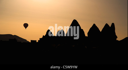 Turchia, Cappadocia, Goreme, vista di silhouette di roccia forme con una mongolfiera in distanza. Foto Stock