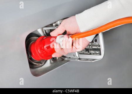 Mano di donna azienda cavo ad alta tensione di caricamento di auto elettriche, close up Foto Stock