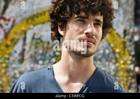 Germania, Berlino, giovane uomo in piedi di fronte a muro con graffiti, ritratto, close-up Foto Stock