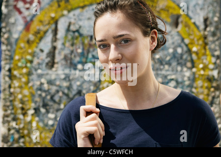 Germania, Berlino, giovane donna in piedi di fronte a muro con graffiti, ritratto, close-up Foto Stock
