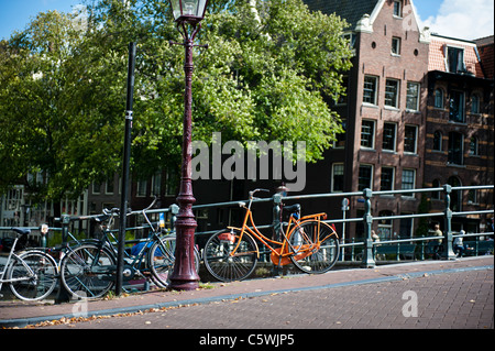 Orange bike incatenati al ponte sul canale Singel in Amsterdam. Il colore arancione è il colore della famiglia reale nei Paesi Bassi. Foto Stock