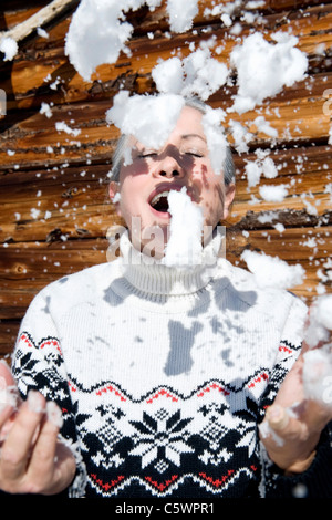 L'Italia, Alto Adige, Seiseralm, Senior donna gettando la neve in aria a occhi chiusi, ritratto Foto Stock