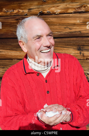 L'Italia, Alto Adige, Seiseralm, Senior man tenendo la neve in mani, ridere, ritratto Foto Stock