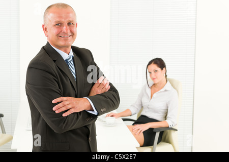 Professional senior imprenditore maturo in piedi in ufficio con attraente segretario Foto Stock