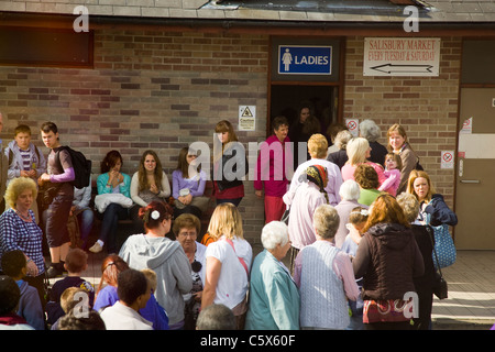 La folla e lunga coda al di fuori di un signore wc in una stazione di servizio Foto Stock