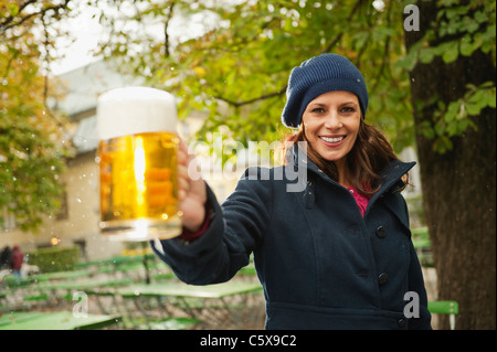 In Germania, in Baviera, Monaco di Baviera, il Giardino Inglese donna nel giardino della birra azienda boccale di birra, sorridente, ritratto Foto Stock