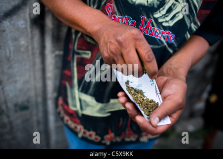 Un messicano seguace di santa muerte (saint morte) rotoli di un giunto di marijuana durante il pellegrinaggio in tepito, Città del Messico. Foto Stock