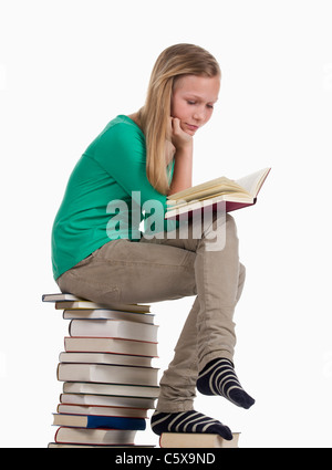 Ragazza seduta e la lettura sulla pila di libri contro uno sfondo bianco Foto Stock