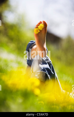 Persona relax nel prato, fiori di dente di leone tra le dita dei piedi Foto Stock