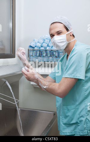 Giovane maschio medico indossando maschera e lavaggio mani Foto Stock
