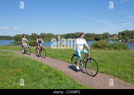 Tre ragazze in bicicletta sulla diga accanto al lago Gartow, Riserva Naturale Elbufer-Drawehn, Bassa Sassonia, Germania Foto Stock