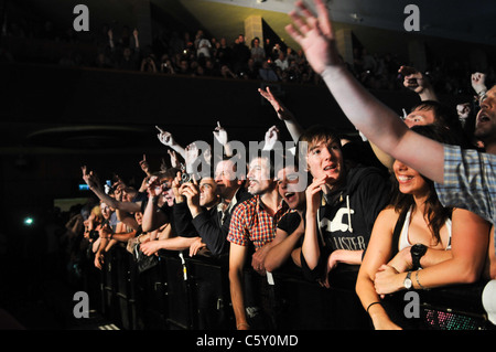 Caldo, sudato giovani tifo folla presso la parte anteriore di un concerto di musica premendo contro una barriera urlando in una band dal vivo sul palco Foto Stock