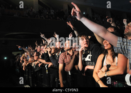 Caldo, sudato giovani tifo folla presso la parte anteriore di un concerto di musica premendo contro una barriera urlando in una band dal vivo sul palco Foto Stock