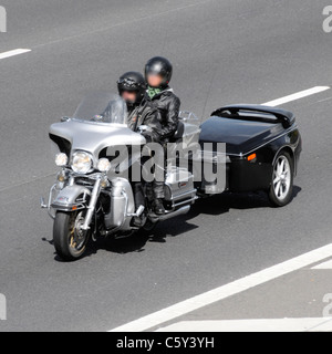 Maschio pilota di moto e donna pillion passeggero che indossa caschi (oscurato volti) con rimorchio percorrendo l autostrada del Regno Unito Foto Stock